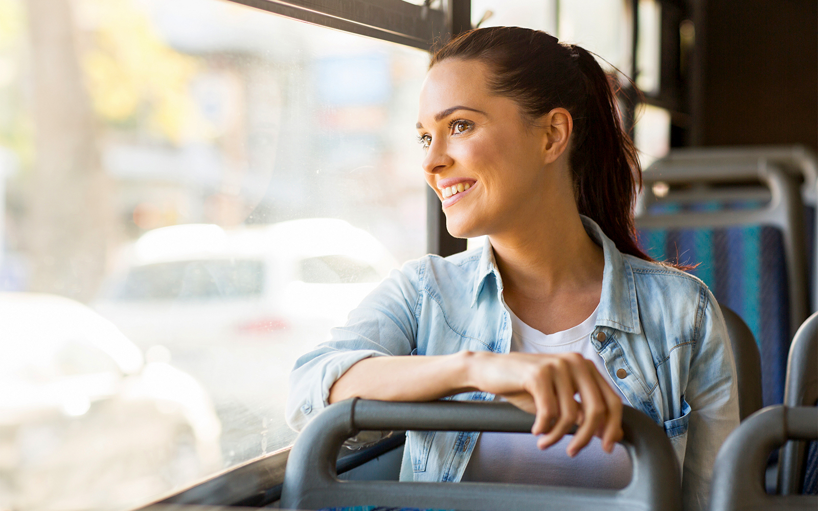 Young woman smiling while riding a bus, looking out the window.