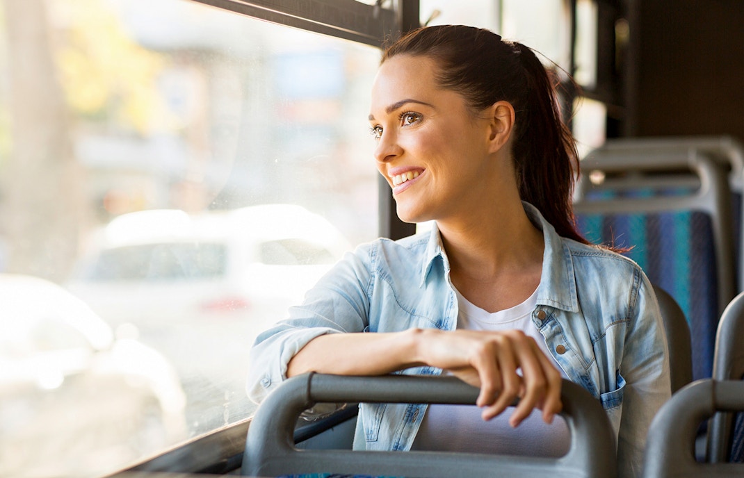 Young woman smiling while riding a bus, looking out the window.