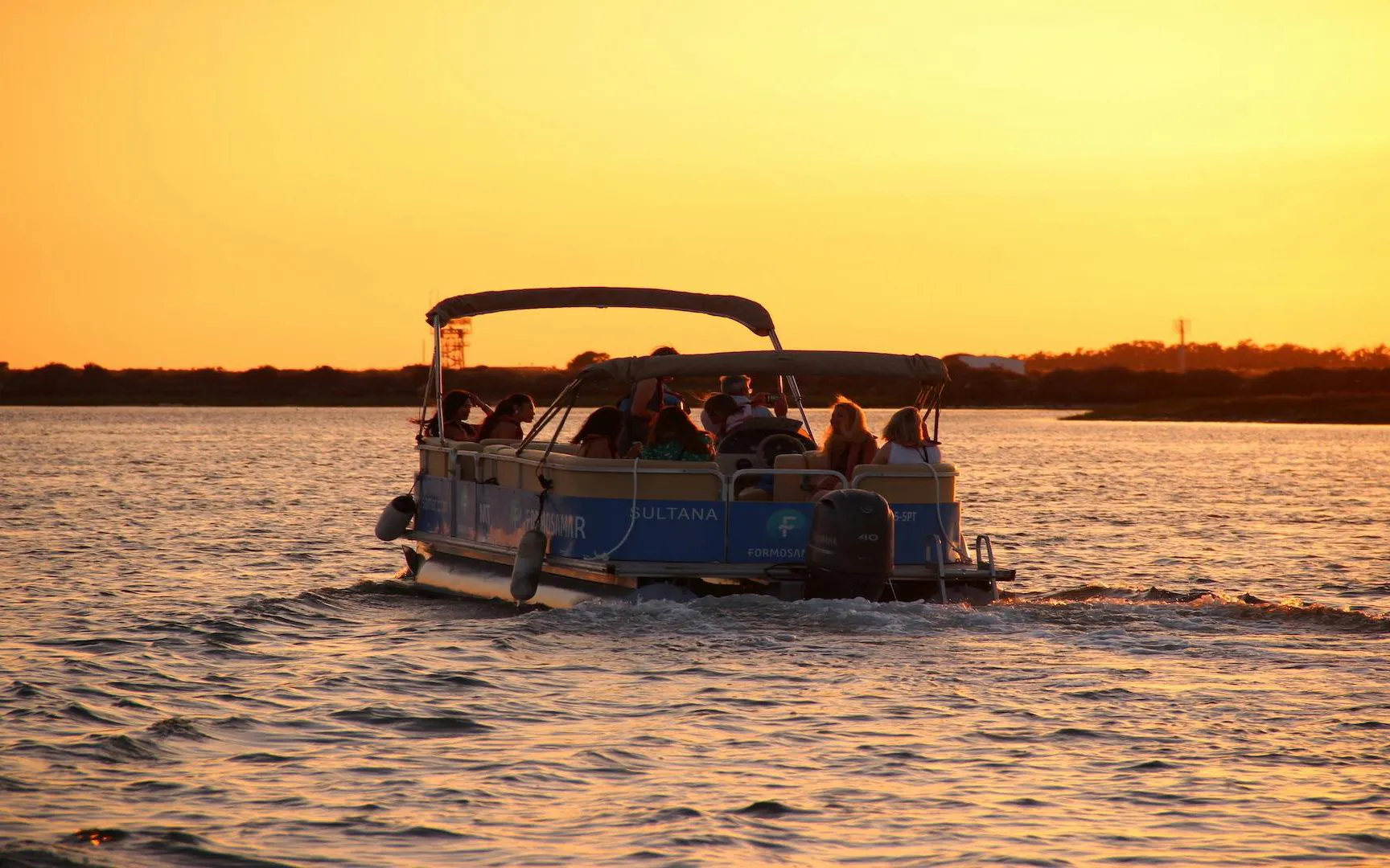 Boat with passengers on Ria Formosa during sunset tour.