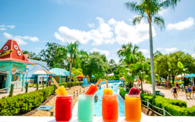 Colorful drinks with popsicles at Adventure Island, Tampa, with a water park and palm trees in the background.