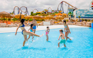 Families enjoying the wave pool at Parque Warner Beach with roller coasters in the background.