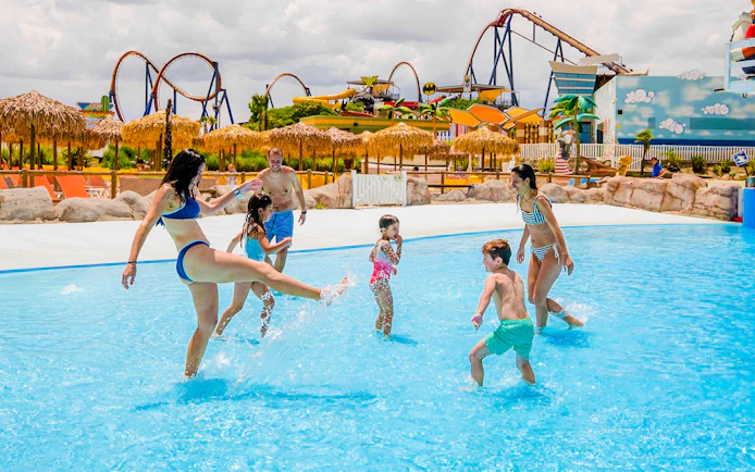 Families enjoying the wave pool at Parque Warner Beach with roller coasters in the background.