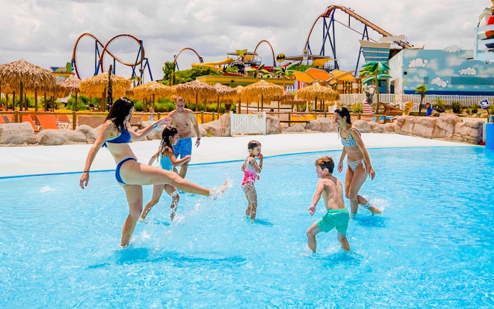 Families enjoying the wave pool at Parque Warner Beach with roller coasters in the background.