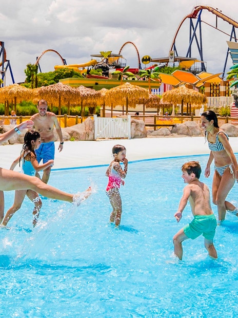 Families enjoying the wave pool at Parque Warner Beach with roller coasters in the background.