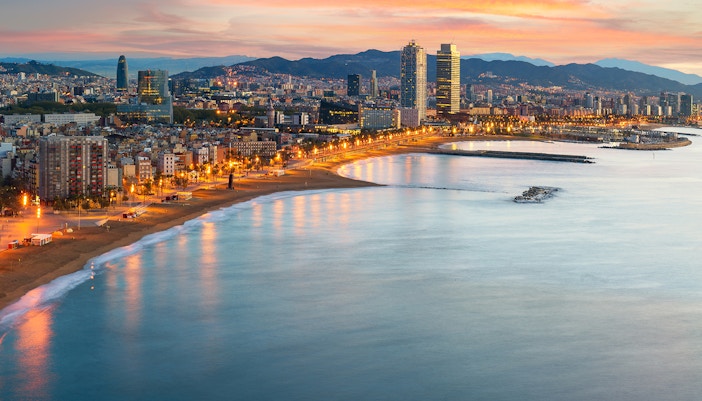 Barcelona beach with people sunbathing and swimming, city skyline in the background.