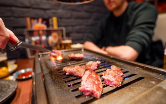 Grilling A5 Wagyu beef on a tabletop grill during Tokyo Omakase Sushi & Foodie Tour in Shinjuku.