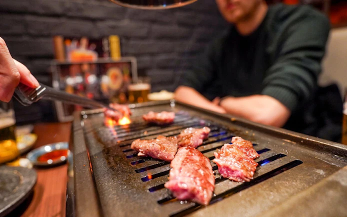 Grilling A5 Wagyu beef on a tabletop grill during Tokyo Omakase Sushi & Foodie Tour in Shinjuku.