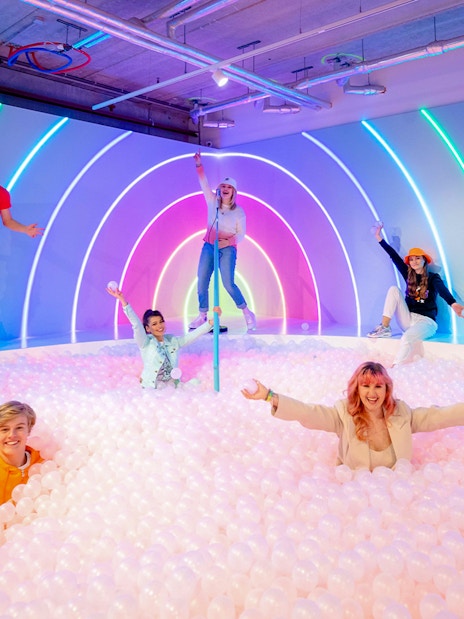 Visitors enjoying The Pool Upside Down Amsterdam with neon lights and ball pit.