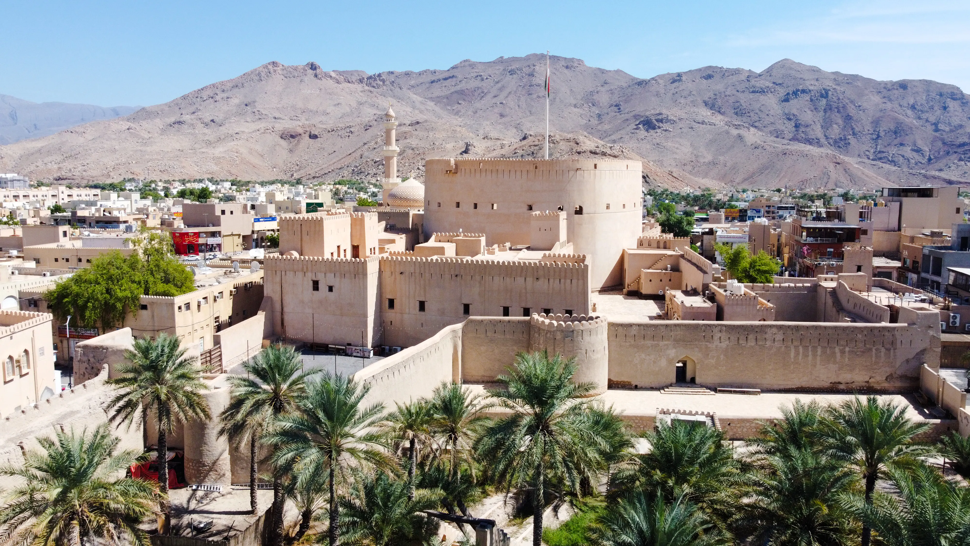 Nizwa Fort with surrounding palm trees and mountains, part of Muscat to Nizwa day trip.