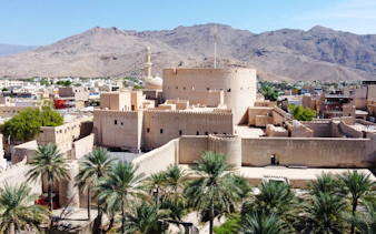 Nizwa Fort with surrounding palm trees and mountains, part of Muscat to Nizwa day trip.