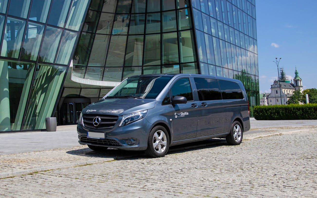 Krakow airport transfer van parked outside modern glass building.