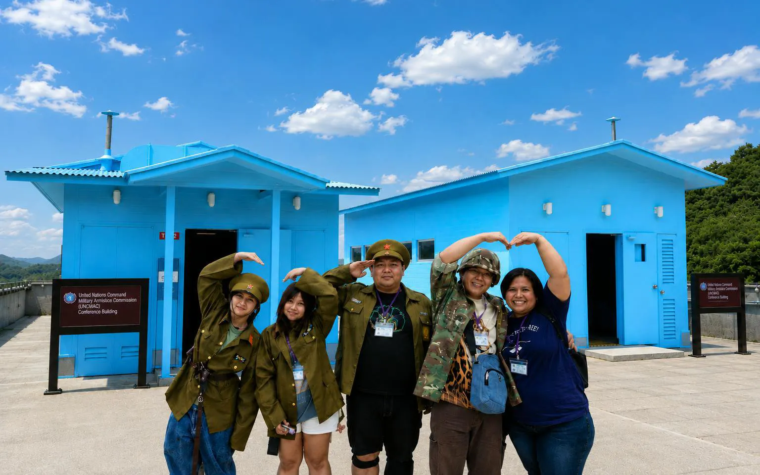 Visitors in military attire pose at the DMZ's JSA Photo Zone, near blue conference buildings.