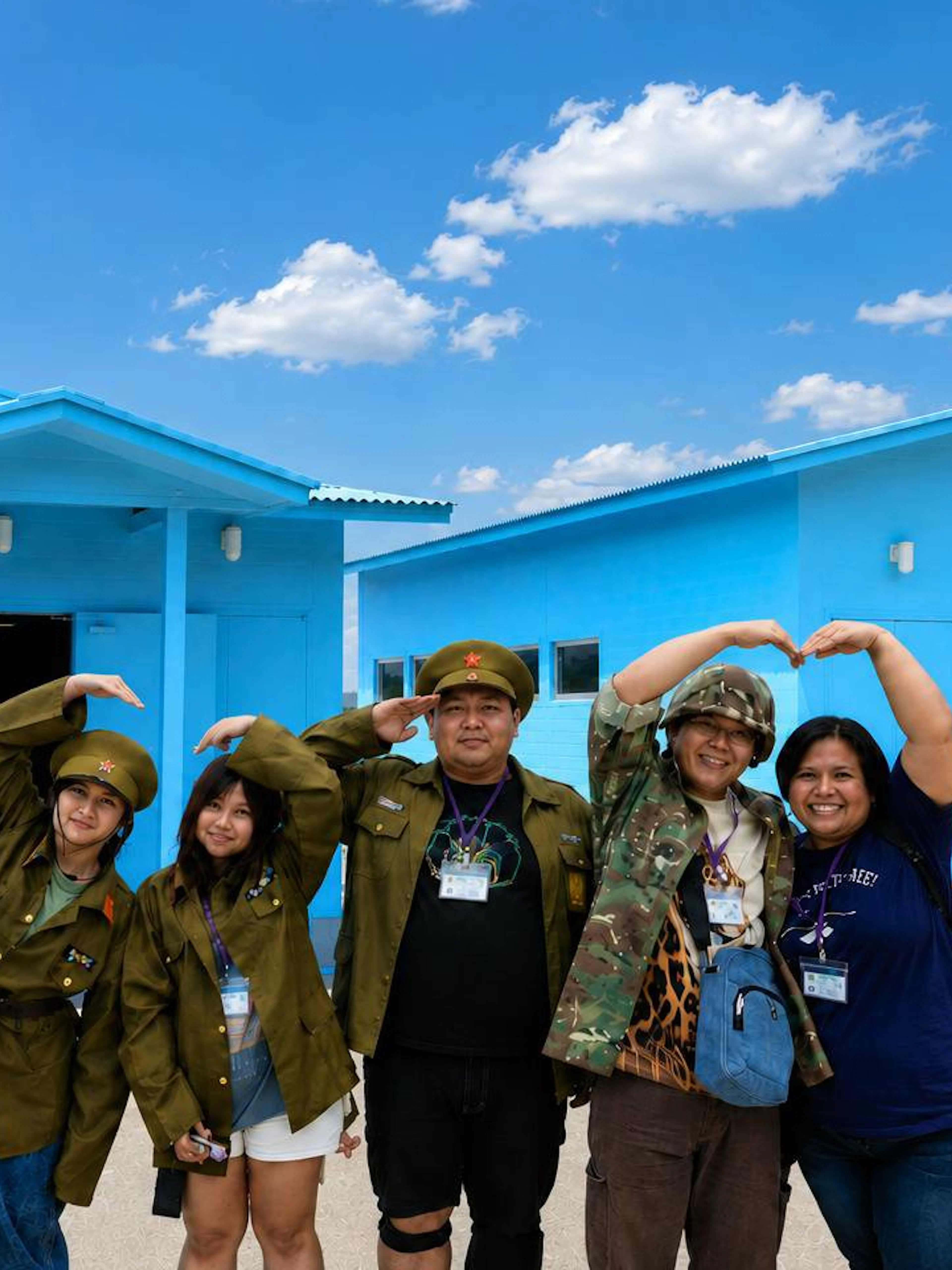 Visitors in military attire pose at the DMZ's JSA Photo Zone, near blue conference buildings.