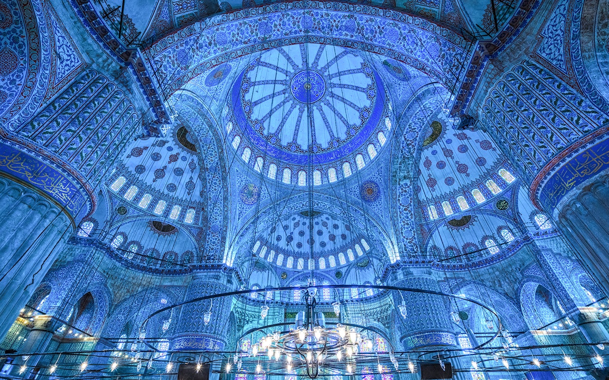 Interior of the Blue Mosque dome in Istanbul, showcasing intricate blue tiles and chandeliers.