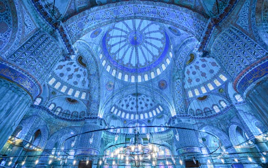 Interior of the Blue Mosque dome in Istanbul, showcasing intricate blue tiles and chandeliers.