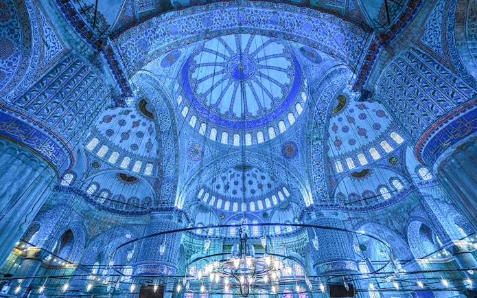 Interior of the Blue Mosque dome in Istanbul, showcasing intricate blue tiles and chandeliers.