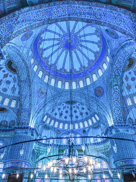 Interior of the Blue Mosque dome in Istanbul, showcasing intricate blue tiles and chandeliers.