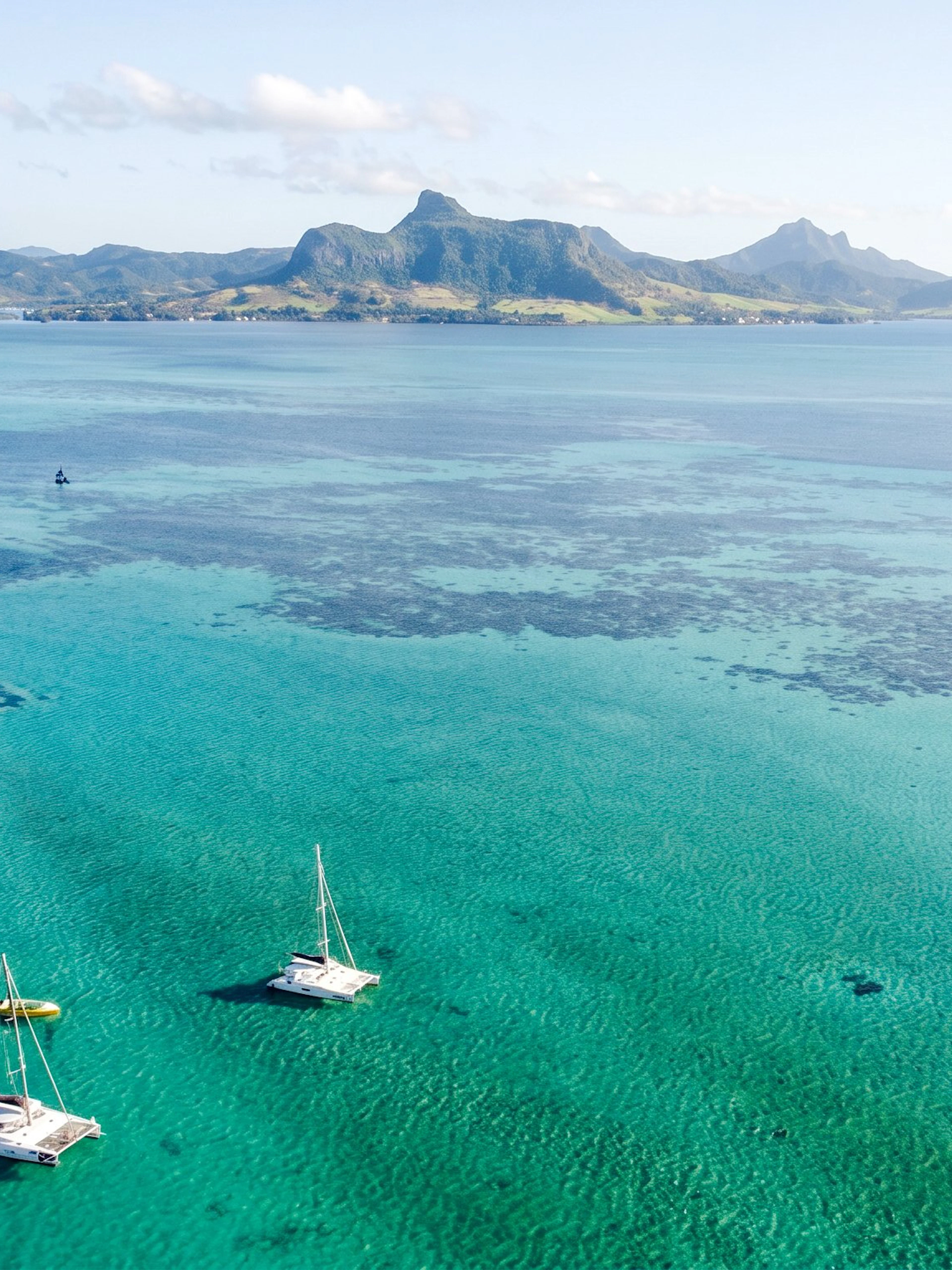 Catamarans sailing to Ile aux Cerfs from Pointe Jerome, Mauritius, with scenic mountain backdrop.