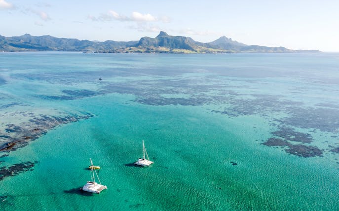 Catamarans sailing to Ile aux Cerfs from Pointe Jerome, Mauritius, with scenic mountain backdrop.