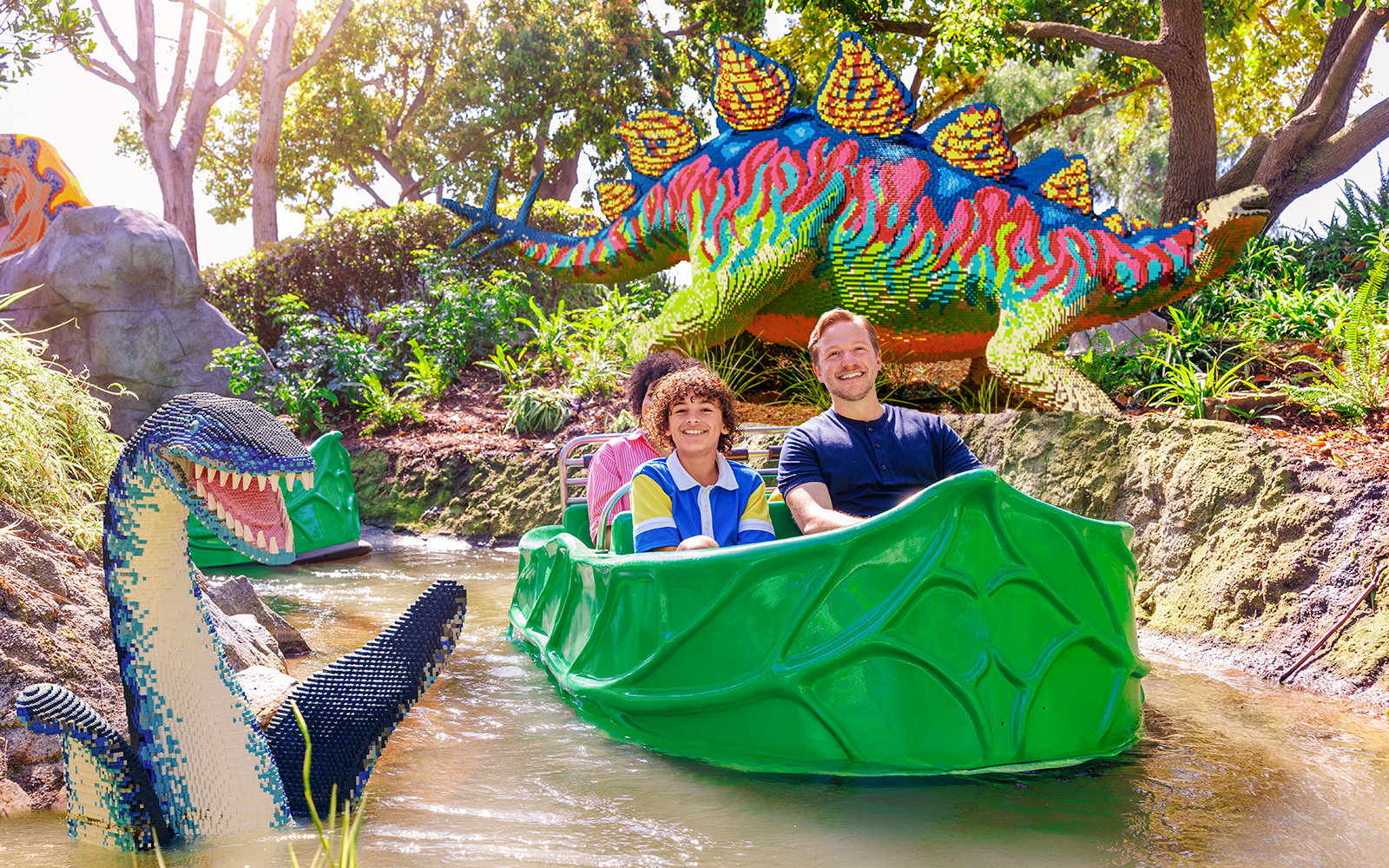 Family enjoying a boat ride past LEGO dinosaur sculptures at LEGOLAND® California.