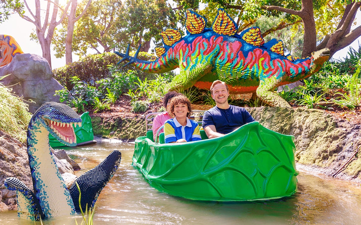 Family enjoying a boat ride past LEGO dinosaur sculptures at LEGOLAND® California.