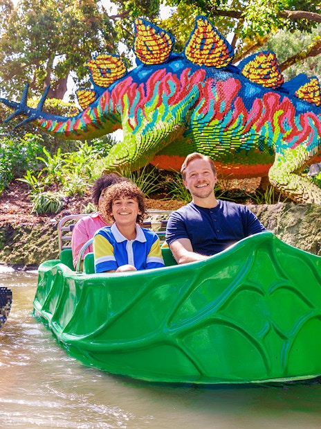 Family enjoying a boat ride past LEGO dinosaur sculptures at LEGOLAND® California.