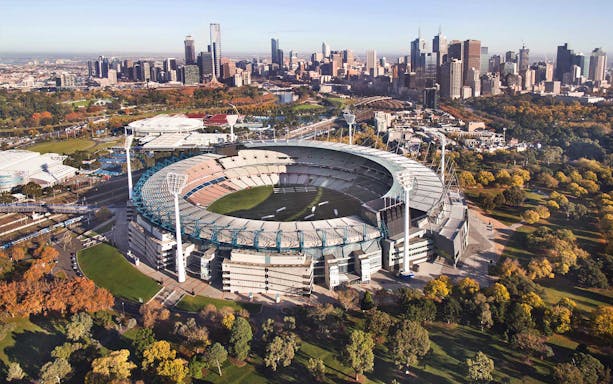 Aerial view of Melbourne Cricket Ground with city skyline in the background.