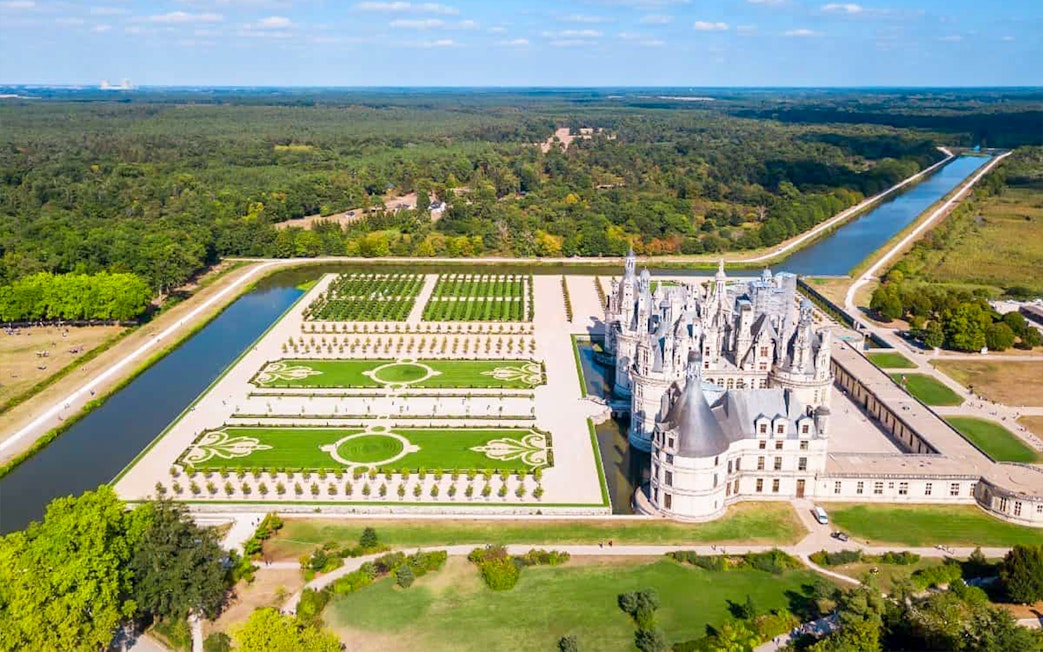 Aerial view of Chambord Castle Gardens with symmetrical landscaping and surrounding canal.