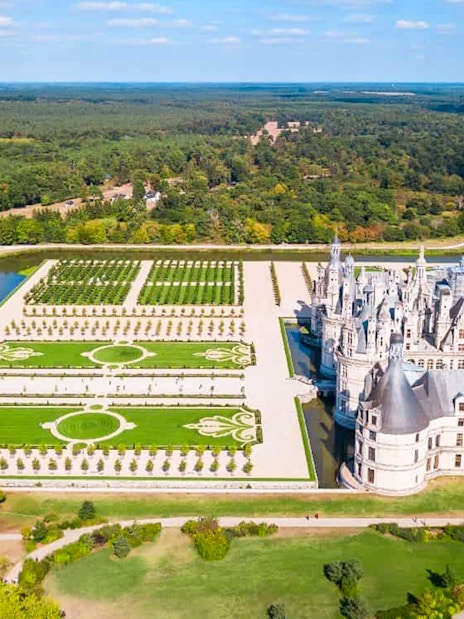 Aerial view of Chambord Castle Gardens with symmetrical landscaping and surrounding canal.