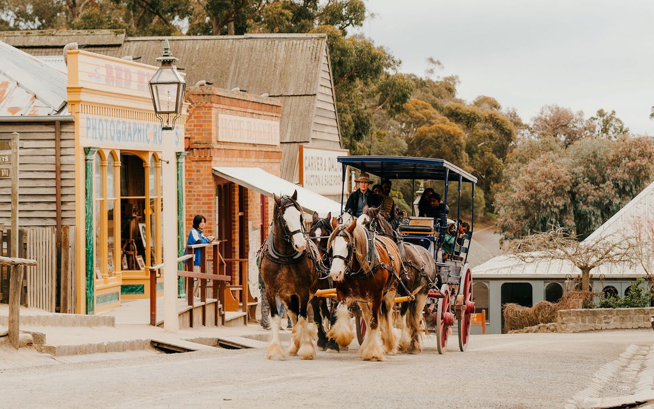 Horse-drawn carriage on street outside Sovereign Hill Museum, showcasing historical buildings.
