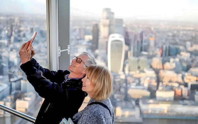 Couple taking a selfie at a London skyscraper with cityscape view.