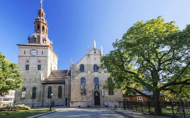 Oslo Cathedral with clock tower and trees on a sunny day, Oslo Walking Tour.