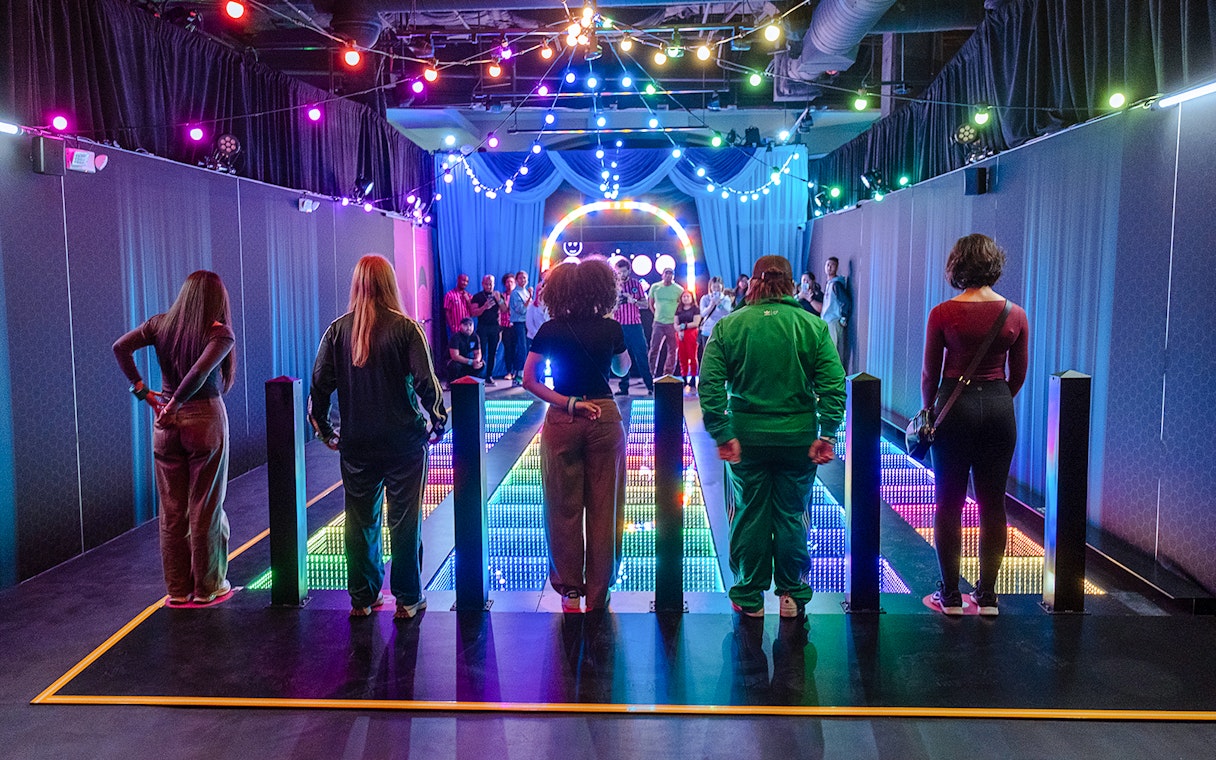 Participants stand on a colorful glass bridge at the Squid Games experience in London.