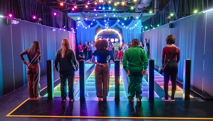 Participants stand on a colorful glass bridge at the Squid Games experience in London.