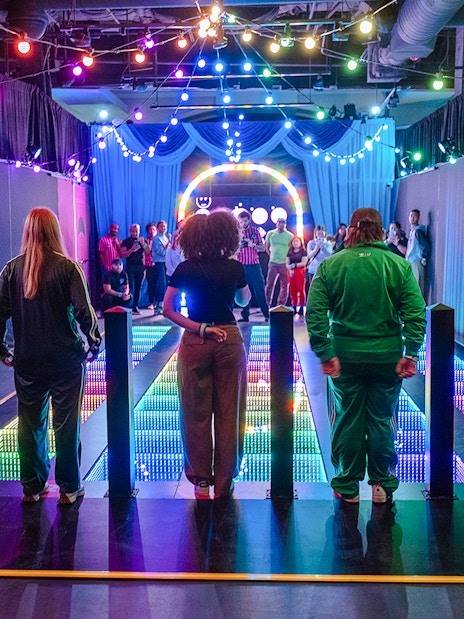 Participants stand on a colorful glass bridge at the Squid Games experience in London.