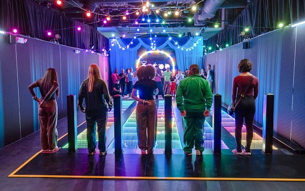 Participants stand on a colorful glass bridge at the Squid Games experience in London.