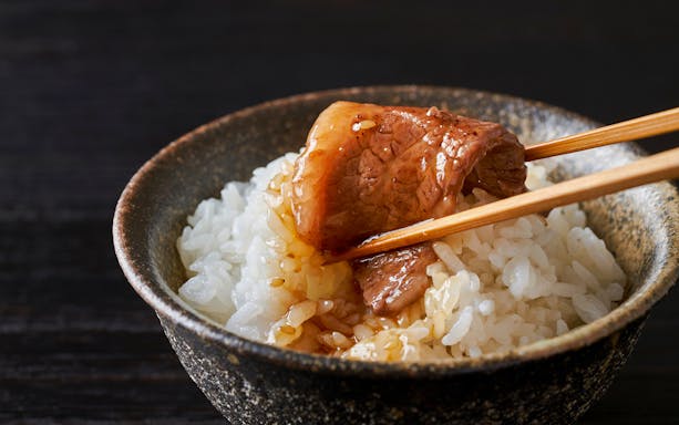 Yakiniku beef slice over rice with chopsticks in a bowl.