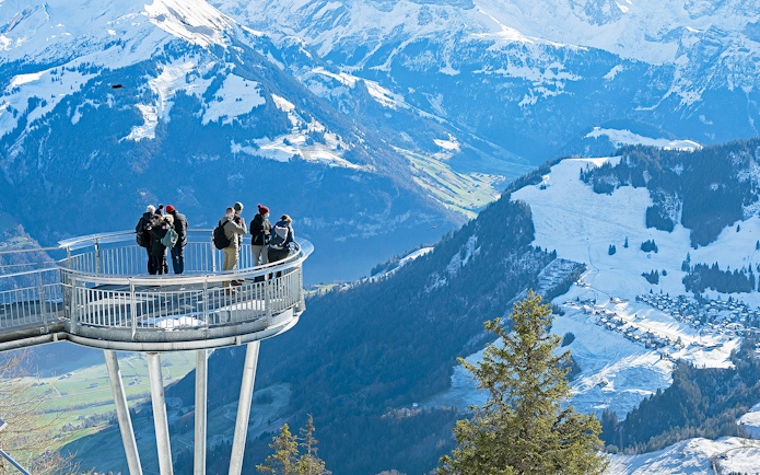 Visitors on Stanserhorn viewing platform overlooking snowy Swiss Alps.