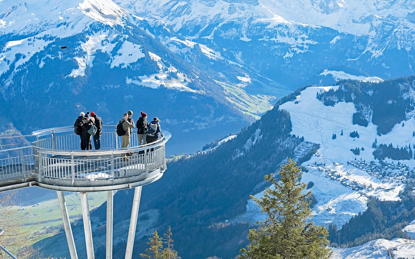 Visitors on Stanserhorn viewing platform overlooking snowy Swiss Alps.