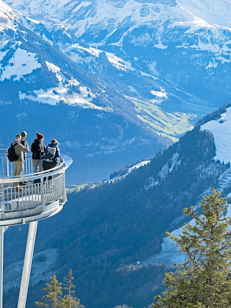 Visitors on Stanserhorn viewing platform overlooking snowy Swiss Alps.