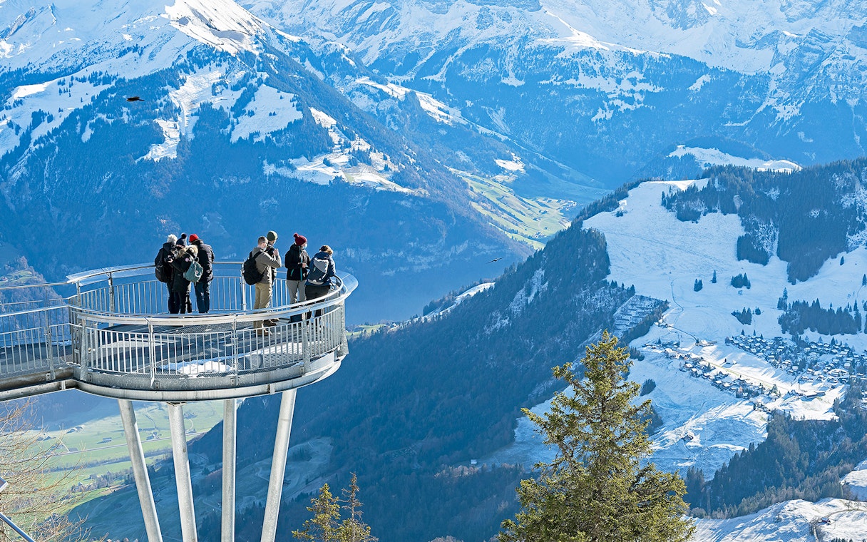 Visitors on Stanserhorn viewing platform overlooking snowy Swiss Alps.