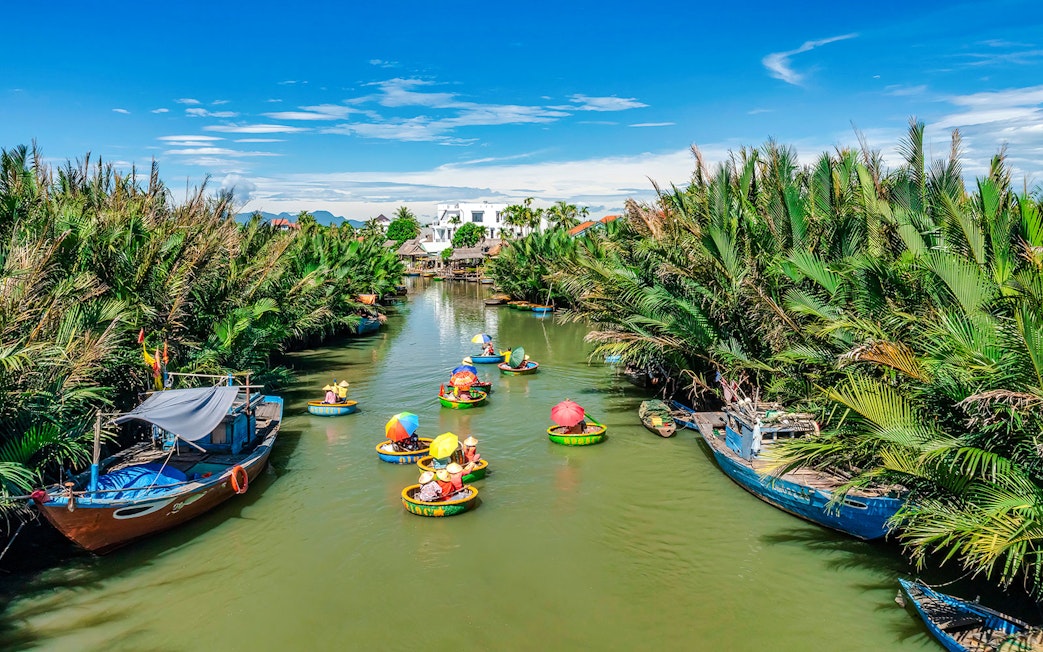 People in round bamboo boats on a river in Cam Thanh Village, surrounded by lush greenery.
