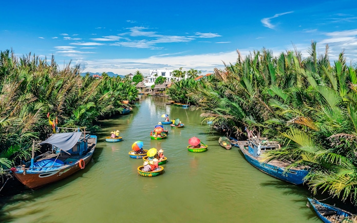 People in round bamboo boats on a river in Cam Thanh Village, surrounded by lush greenery.