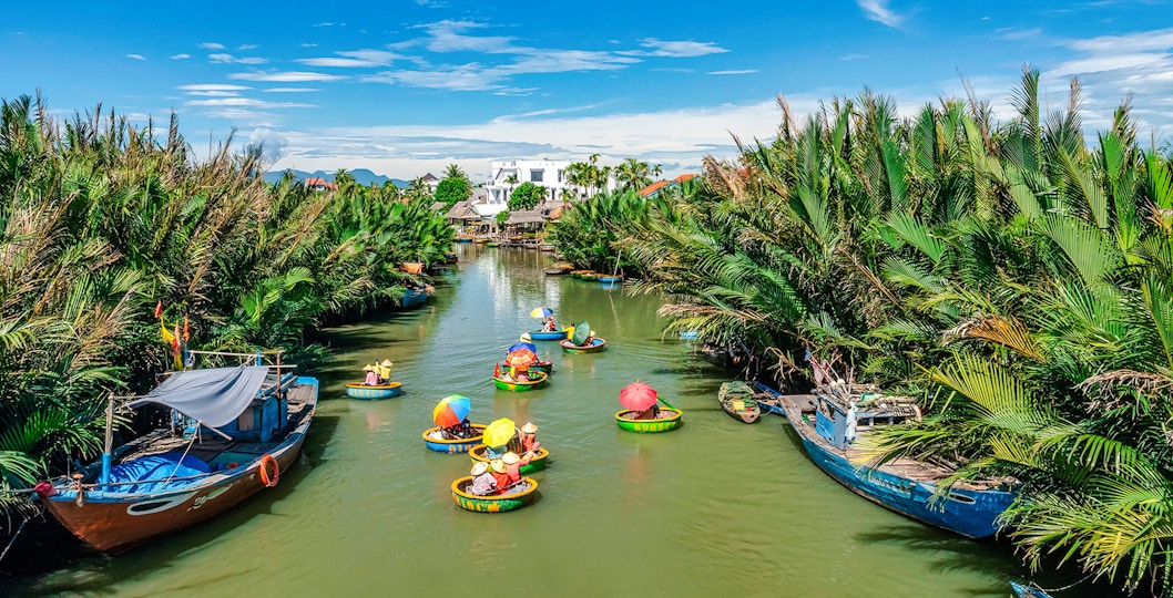 People in round bamboo boats on a river in Cam Thanh Village, surrounded by lush greenery.