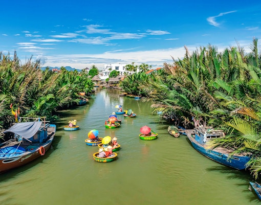 People in round bamboo boats on a river in Cam Thanh Village, surrounded by lush greenery.