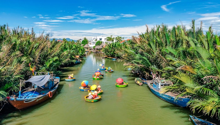 People in round bamboo boats on a river in Cam Thanh Village, surrounded by lush greenery.