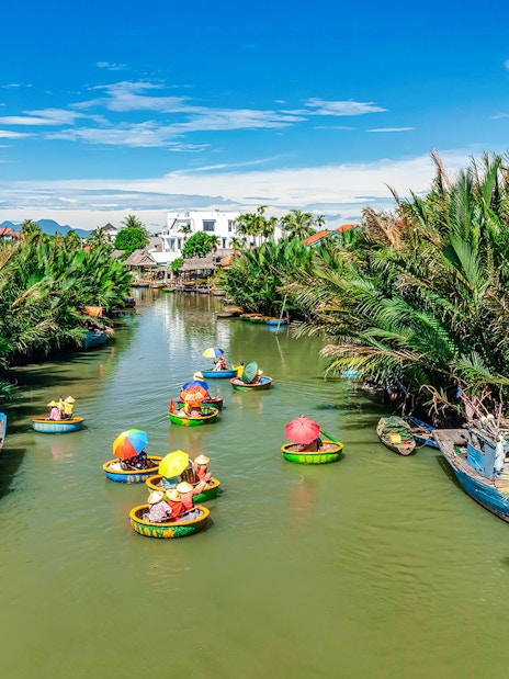 People in round bamboo boats on a river in Cam Thanh Village, surrounded by lush greenery.