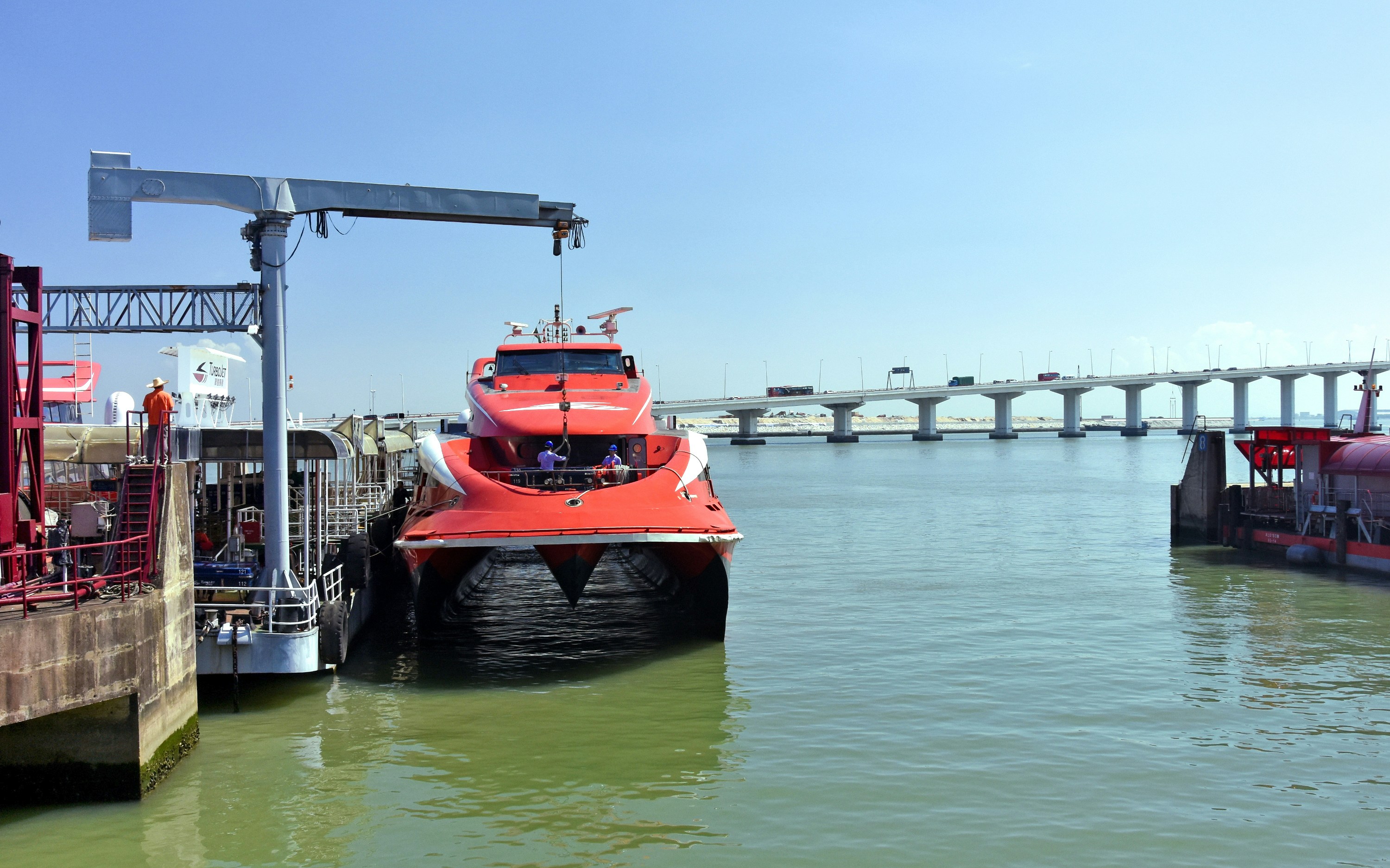 Turbojet boat docked at Macau Ferry Terminal with bridge in background.