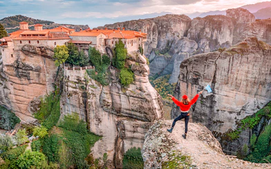 Tourist with Greek flag admiring Meteora rock formations and monastery, Greece.