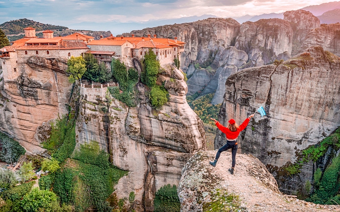 Tourist with Greek flag admiring Meteora rock formations and monastery, Greece.